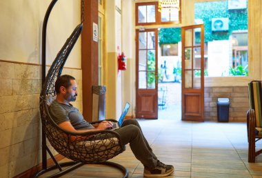 Yetişkin Latin Amerikalı bir adam bir yurtta dizüstü bilgisayarıyla çalışıyor. dijital göçebe