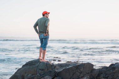 Gün batımında plajda tek başına duran beyaz bir adam.