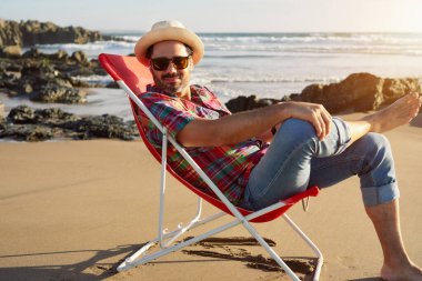 Olgun bir adam plajda oturmuş yalnızlığın ve günbatımının tadını çıkarıyor.