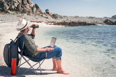 Kumsalda dizüstü bilgisayarı ve bir şişe birası olan bir yürüyüşçü.