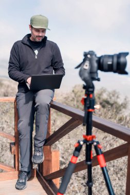 Elinde laptop ve fotoğraf makinesi olan olgun bir insan Pasifik Okyanusu 'nun üzerinde gözetleme noktasında oturuyor. 