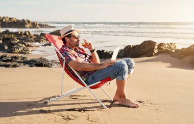 Kumsalda oturan mutlu, olgun bir adam kollarını kaldırıp bira ve yalnızlığın tadını çıkarıyor.