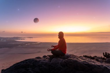 Bir insanın silueti dağın tepesinde oturmuş gün batımında şehir ve okyanus üzerinde meditasyon yapıyor..