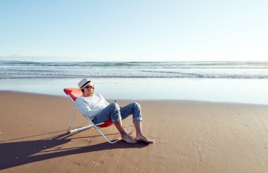 Plaj sandalyesinde oturmuş bira içen olgun Latin bir adam. 
