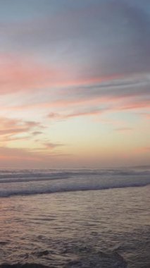 Renkli gün batımı gökyüzü ve kumlu sahilde okyanus dalgaları.