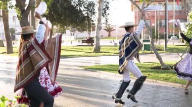 Şehir meydanında geleneksel huaso kıyafetleri içinde dans eden iki çiftin portresi.