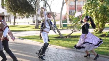 Şehir meydanında geleneksel huaso kıyafetleri içinde dans eden iki çiftin portresi.