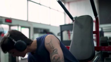 Kulaklıklı genç erkek sporcu spor aletleri kullanarak, kas gelişimine ve fitness 'e odaklanarak, güçlü eğitim egzersizleri yapıyor.