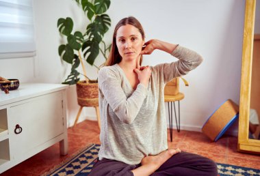 Kadın oturma odasında boynuna yoga egzersizleri yapıyor.