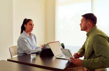 İki iş adamı bir masada dizüstü bilgisayar ve tablet kullanarak toplantı sırasında tartışıyorlar.