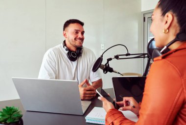 İki içerik oluşturucu profesyonel mikrofon ve dizüstü bilgisayar kullanarak bir ev stüdyosunda bir podcast kaydediyor.