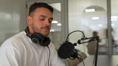 Beyaz tişörtlü bir adam stüdyoda ses yayını kaydediyordu. Laptop kullanıyordu ve konuğuyla konuşuyordu. 