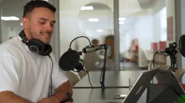 İki radyo sunucusu bir stüdyoda canlı yayın sırasında sohbet ediyorlar. Masada oturan kulaklık takan erkek ve kadın kayıt için dizüstü bilgisayar ve tablet bilgisayar kullanıyor. 