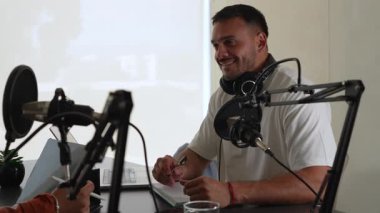 İki radyo sunucusu bir stüdyoda canlı yayında dizüstü bilgisayar kullanıyor ve tartışıyorlar.