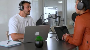 İki radyo sunucusu bir stüdyoda canlı yayında dizüstü bilgisayar kullanıyor ve tartışıyorlar.