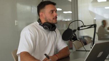 Beyaz tişörtlü bir adam stüdyoda ses yayını kaydediyordu. Laptop kullanıyordu ve konuğuyla konuşuyordu. 