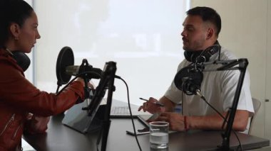 İki radyo sunucusu bir stüdyoda canlı yayında dizüstü bilgisayar kullanıyor ve tartışıyorlar.