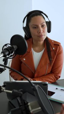 Latin kadın stüdyoda iş arkadaşını dinlerken podcast ses kaydı yapıyor.