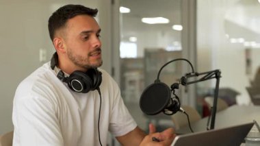 Beyaz tişörtlü bir adam stüdyoda ses yayını kaydediyordu. Laptop kullanıyordu ve konuğuyla konuşuyordu. 