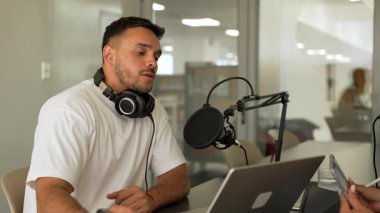 Beyaz tişörtlü bir adam stüdyoda ses yayını kaydediyordu. Laptop kullanıyordu ve konuğuyla konuşuyordu. 