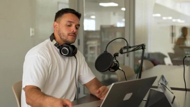 Beyaz tişörtlü bir adam stüdyoda ses yayını kaydediyordu. Laptop kullanıyordu ve konuğuyla konuşuyordu. 