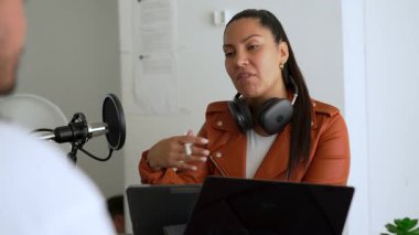 İki radyo sunucusu bir stüdyoda canlı yayın sırasında sohbet ediyorlar. Masada oturan kulaklık takan erkek ve kadın kayıt için dizüstü bilgisayar ve tablet bilgisayar kullanıyor. 