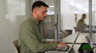 Genç adam ofiste dizüstü bilgisayar kullandıktan sonra esneme hareketleri yapıyor.