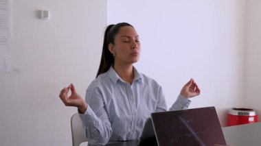 Genç iş kadını ofisinde meditasyon yapıyor. Masasında tabletinin önünde oturuyor. 