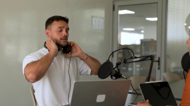 İki radyo sunucusu bir stüdyoda canlı yayın sırasında sohbet ediyorlar. Masada oturan kulaklık takan erkek ve kadın kayıt için dizüstü bilgisayar ve tablet bilgisayar kullanıyor. 