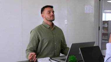 Genç erkek çalışan ofiste meditasyon yapıyor. Masada oturuyor. 