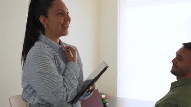 İki iş arkadaşı bir projeyi tartışıyor, fikirleri paylaşıyor, kadın tabletle ayakta duruyor, adam masada oturuyor. 