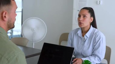 İki iş arkadaşı bir projeyi tartışıyor. Kadın ve erkek, masada oturmuş birbirlerinin önünde aletlerle iletişim kuruyorlar.