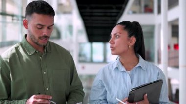 İki yönetici iş projesini tartışıyor ofiste birlikte yürüyor ve notlar alıyorlar.