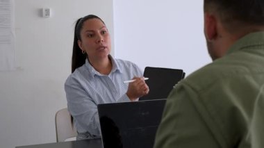 İki iş arkadaşı bir projeyi tartışıyor. Kadın ve erkek, masada oturmuş birbirlerinin önünde aletlerle iletişim kuruyorlar.