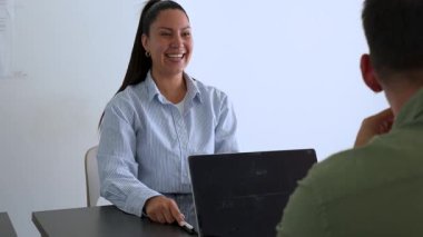 İki iş arkadaşı ofiste eğleniyor, kadın ve erkek masanın önünde oturmuş birbirlerine gülüyorlar. 