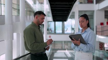 İki yönetici iş projesini tartışıyor ofiste birlikte yürüyor ve notlar alıyorlar.