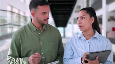 İki yönetici iş projesini tartışıyor ofiste birlikte yürüyor ve notlar alıyorlar.