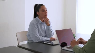 İki iş arkadaşı bir projeyi tartışıyor. Kadın ve erkek, masada oturmuş birbirlerinin önünde aletlerle iletişim kuruyorlar.