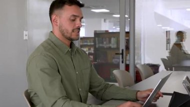 Ofiste dizüstü bilgisayar kullanan ve konuşan yeşil tişörtlü genç bir adamın portresi.