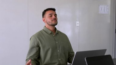 Genç erkek çalışan ofiste meditasyon yapıyor. Masada oturuyor. 