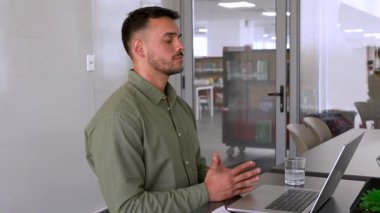 Genç erkek çalışan ofiste meditasyon yapıyor. Masada oturuyor. 