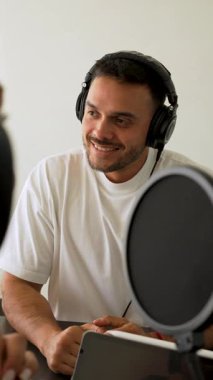 Beyaz tişörtlü bir adam stüdyoda ses yayını kaydediyordu. Laptop kullanıyordu ve konuğuyla konuşuyordu. 