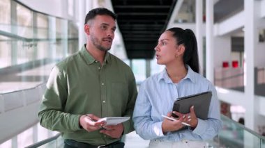İki yönetici iş projesini tartışıyor ofiste birlikte yürüyor ve notlar alıyorlar.