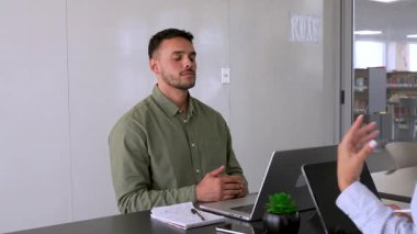 Genç erkek çalışan ofiste meditasyon yapıyor. Masada oturuyor. 