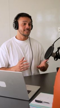 Beyaz tişörtlü bir adam stüdyoda ses yayını kaydediyordu. Laptop kullanıyordu ve konuğuyla konuşuyordu. 