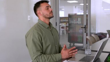 Genç erkek çalışan ofiste meditasyon yapıyor. Masada oturuyor. 