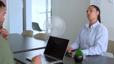 İki iş arkadaşı bir projeyi tartışıyor. Kadın ve erkek, masada oturmuş birbirlerinin önünde aletlerle iletişim kuruyorlar.