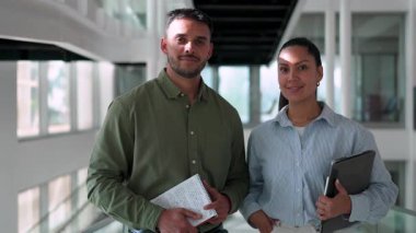 Ofiste birlikte poz verip gülümseyen iki yönetici. Elinde tablet olan kadın ve elinde not defteri tutan adam. 