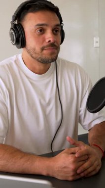 Beyaz tişörtlü bir adam profesyonel ekipman kullanarak stüdyoda ses yayını yapıyor.