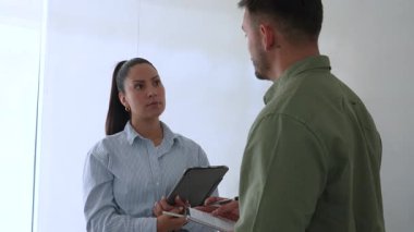 Genç iş çifti ofiste konuşuyor ve notlar alıyor.